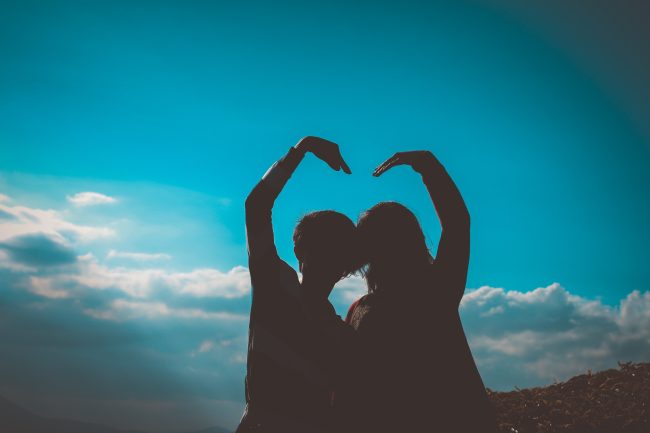 Couple make heart with hands with blue sky showing through heart.