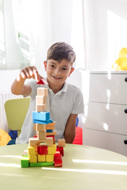 Little boy plays with wooden blocks at children's table in bright room.